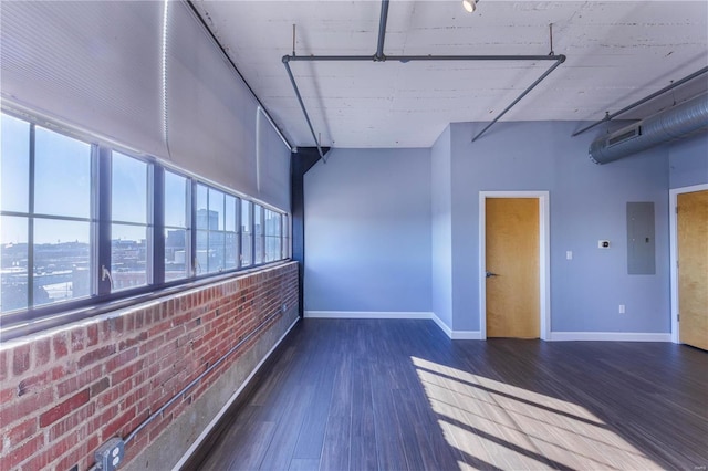 empty room with electric panel, baseboards, a towering ceiling, brick wall, and wood finished floors