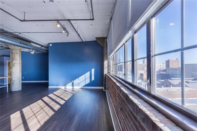 unfurnished room with a view of city, wood finished floors, rail lighting, and baseboards