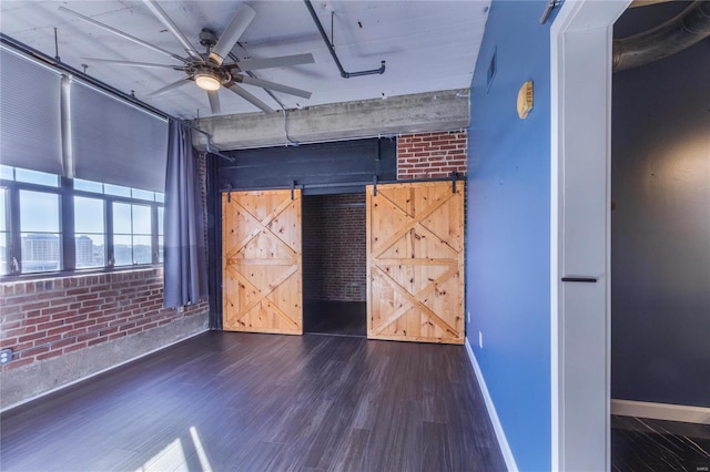 unfurnished bedroom with brick wall, baseboards, dark wood-type flooring, and a barn door