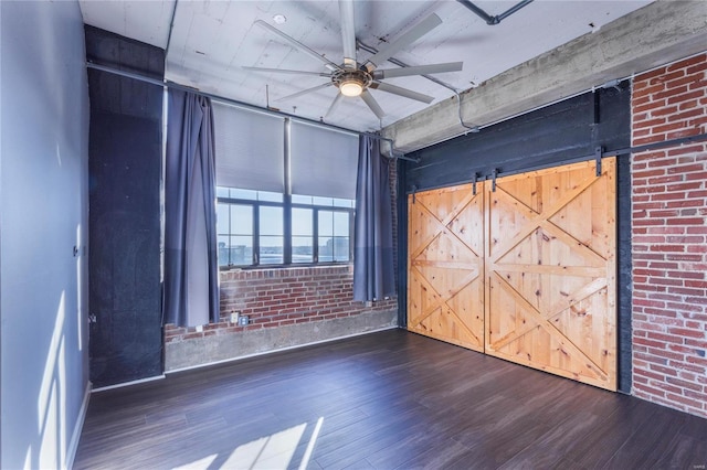 unfurnished bedroom with a ceiling fan, a barn door, brick wall, and wood finished floors