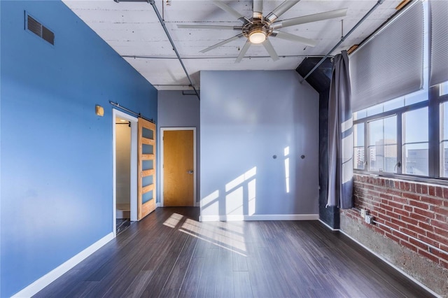 unfurnished room with visible vents, a barn door, a ceiling fan, wood finished floors, and baseboards