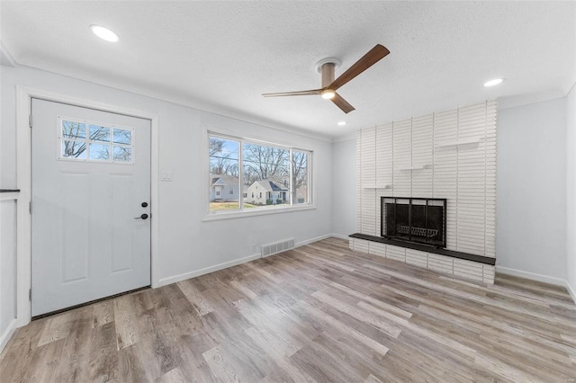 unfurnished living room featuring visible vents, a ceiling fan, a textured ceiling, wood finished floors, and a fireplace