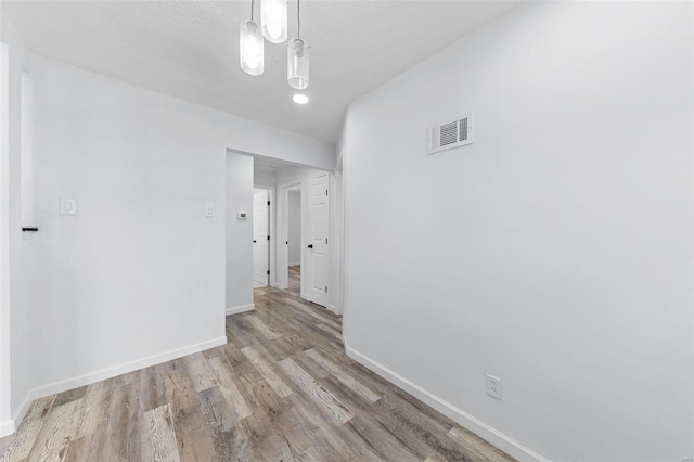 interior space with a textured ceiling, wood finished floors, visible vents, and baseboards