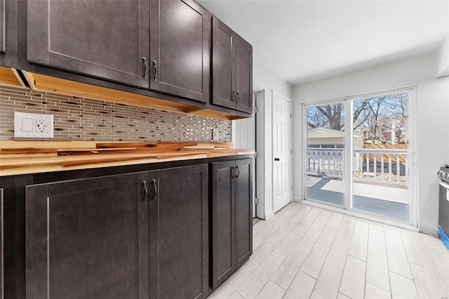 kitchen with dark brown cabinets, baseboards, butcher block countertops, decorative backsplash, and light wood-style floors