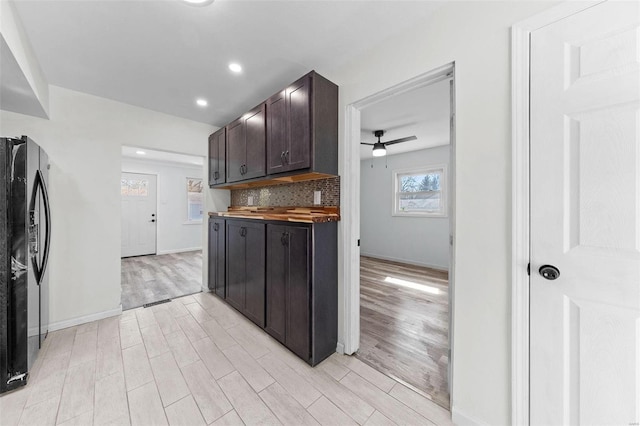 kitchen with a ceiling fan, tasteful backsplash, freestanding refrigerator, light wood-style floors, and dark brown cabinets