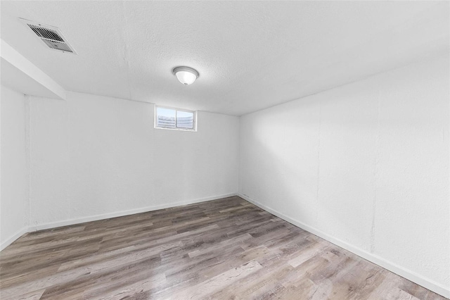 below grade area featuring baseboards, wood finished floors, visible vents, and a textured ceiling