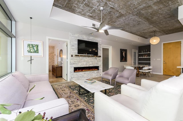 living room featuring ceiling fan, a stone fireplace, wood finished floors, visible vents, and baseboards