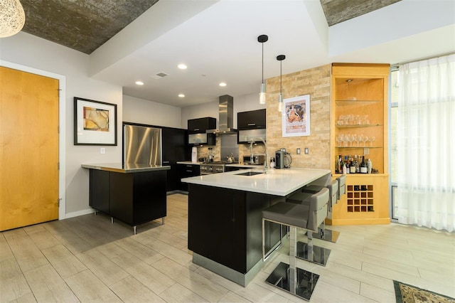 kitchen featuring light countertops, visible vents, dark cabinets, a peninsula, and wall chimney exhaust hood