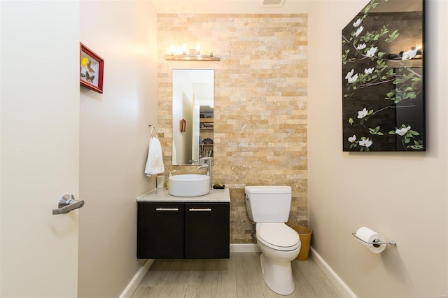 half bathroom with visible vents, baseboards, toilet, vanity, and tile walls