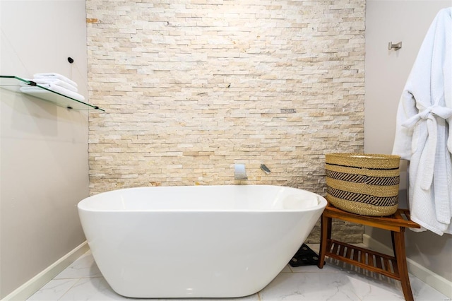 bathroom featuring marble finish floor, a freestanding tub, and baseboards