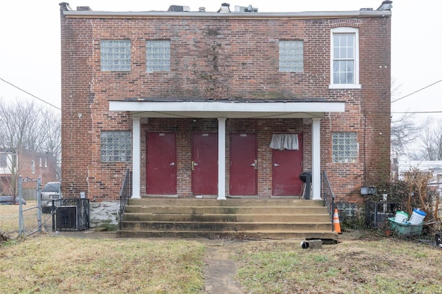 view of front of home featuring brick siding, a front lawn, cooling unit, and fence