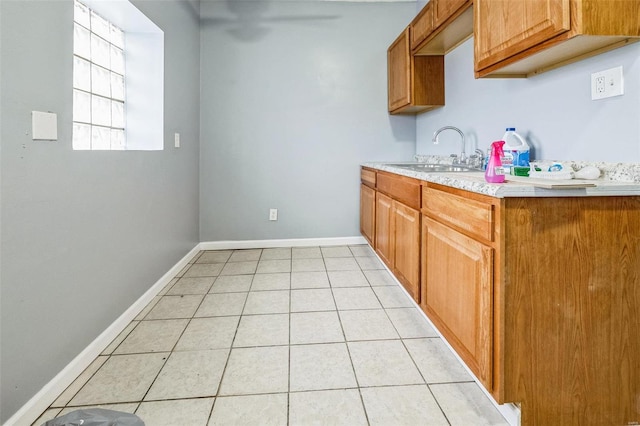 kitchen featuring light tile patterned flooring, a sink, baseboards, light countertops, and brown cabinetry