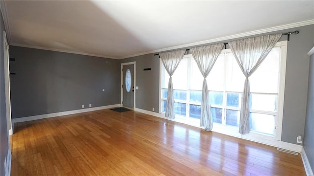 empty room featuring ornamental molding, visible vents, baseboards, and wood finished floors