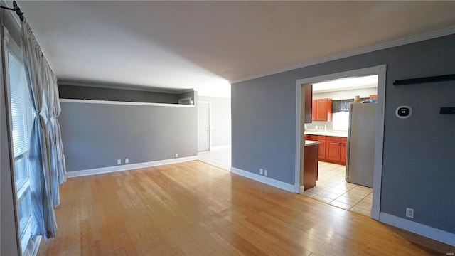 interior space with light wood-style flooring, baseboards, crown molding, and freestanding refrigerator