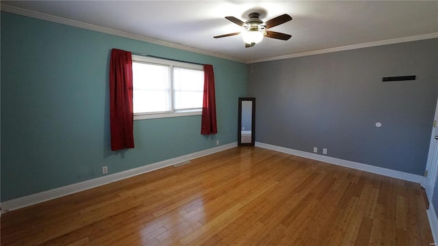 empty room with baseboards, crown molding, visible vents, and wood finished floors