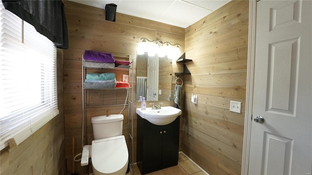 half bathroom featuring tile patterned flooring, wooden walls, toilet, and vanity