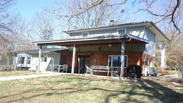 back of property with a lawn, ceiling fan, a chimney, central AC, and brick siding