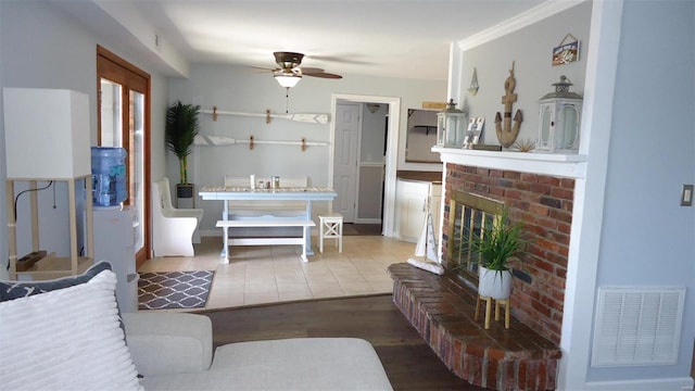 living room featuring visible vents, a ceiling fan, ornamental molding, wood finished floors, and a brick fireplace