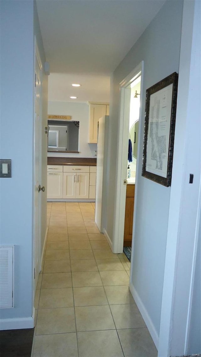 hallway with light tile patterned floors, visible vents, and baseboards