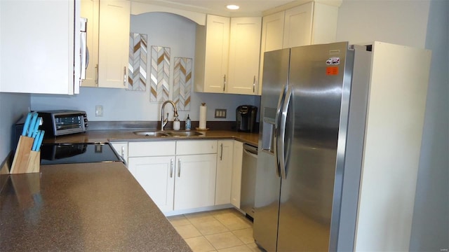 kitchen featuring stainless steel appliances, dark countertops, a sink, and white cabinetry