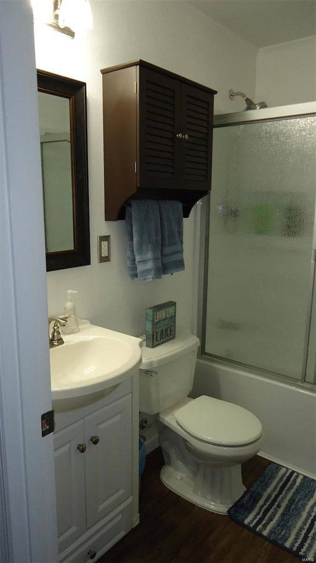 bathroom featuring toilet, bath / shower combo with glass door, wood finished floors, and vanity