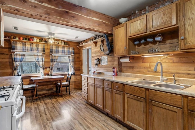 kitchen with light wood finished floors, white gas range oven, light countertops, wood walls, and a sink