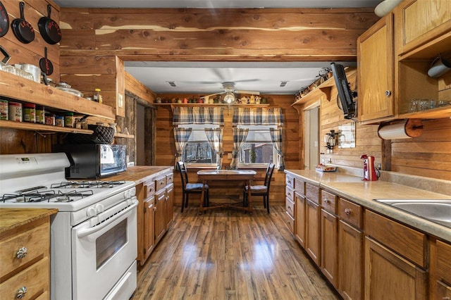 kitchen featuring white range with gas cooktop, wood finished floors, light countertops, wood walls, and open shelves