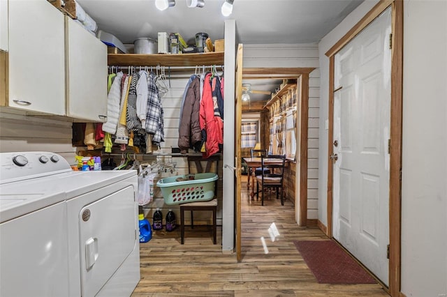 washroom with cabinet space, separate washer and dryer, light wood-style floors, and wood walls