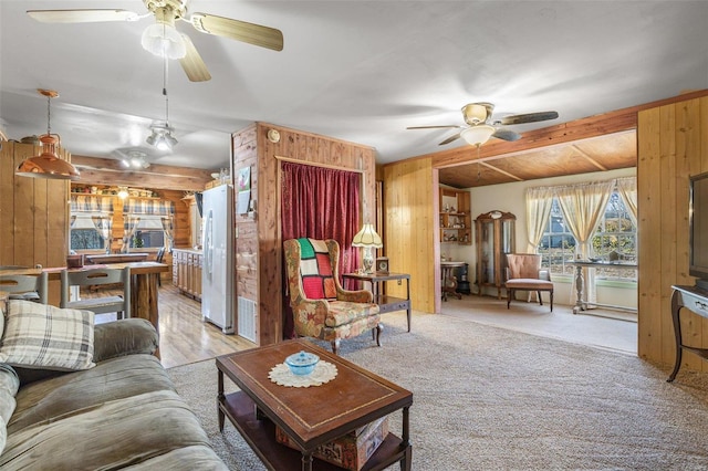 living area with a ceiling fan, light colored carpet, and wood walls