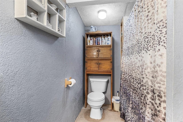 bathroom with toilet, a textured ceiling, and a textured wall