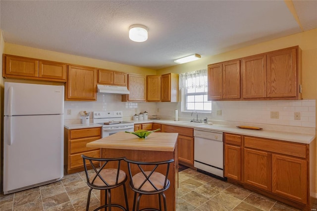 kitchen with white appliances, under cabinet range hood, decorative backsplash, and a sink