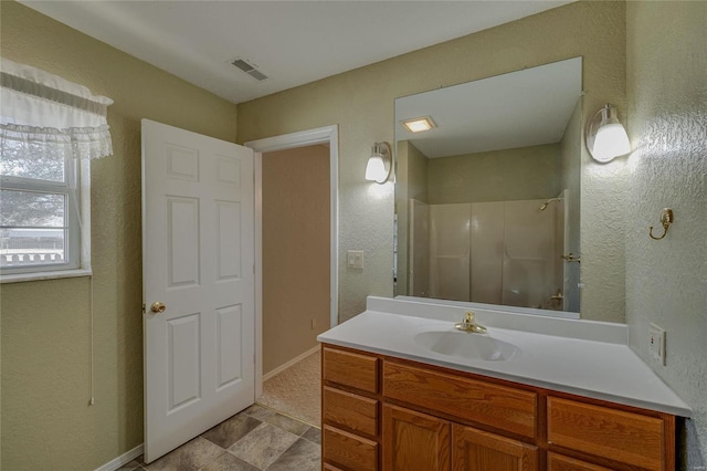 full bathroom with a textured wall, vanity, visible vents, baseboards, and walk in shower