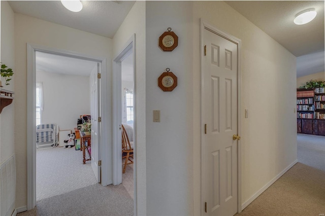 hallway featuring light carpet, visible vents, and baseboards