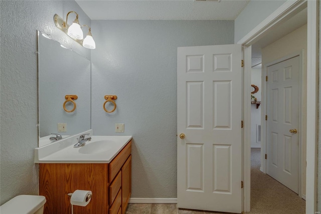 bathroom featuring toilet, a textured wall, visible vents, and vanity