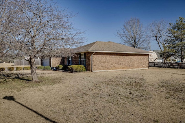 view of side of home with roof with shingles, fence, and brick siding