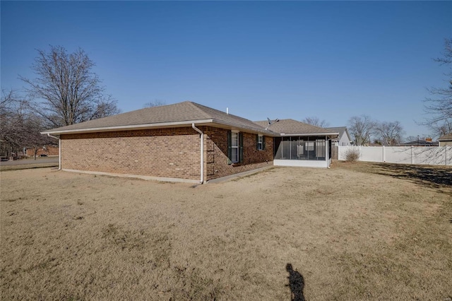 rear view of property featuring a shingled roof, a lawn, a sunroom, fence, and brick siding