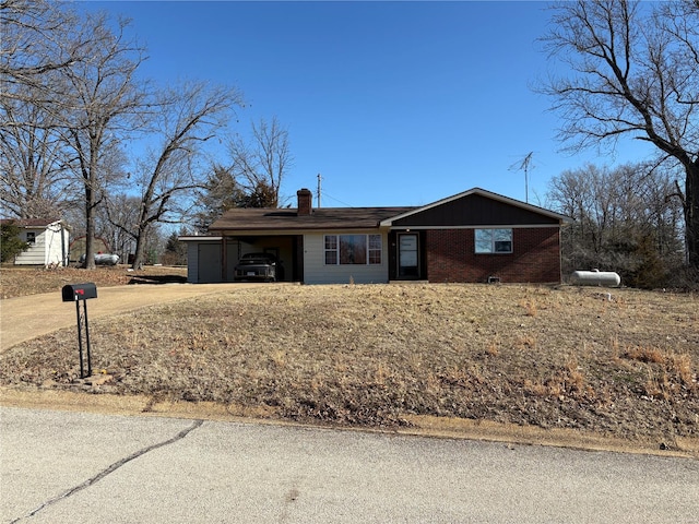 ranch-style house featuring an attached carport, brick siding, driveway, and a chimney