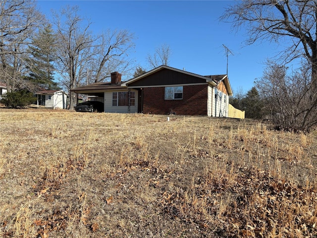 view of front of home featuring a chimney, an attached carport, and brick siding