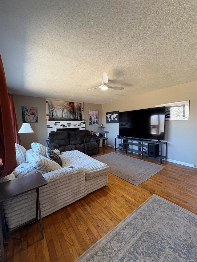 living area with a ceiling fan, wood-type flooring, a textured ceiling, and baseboards