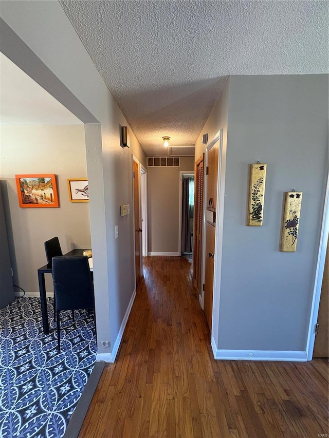 hall featuring wood-type flooring, visible vents, baseboards, and a textured ceiling