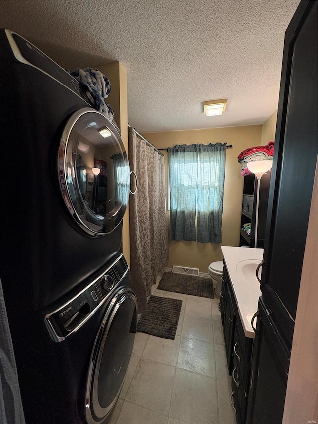 laundry area with light tile patterned floors, visible vents, a textured ceiling, stacked washing maching and dryer, and laundry area