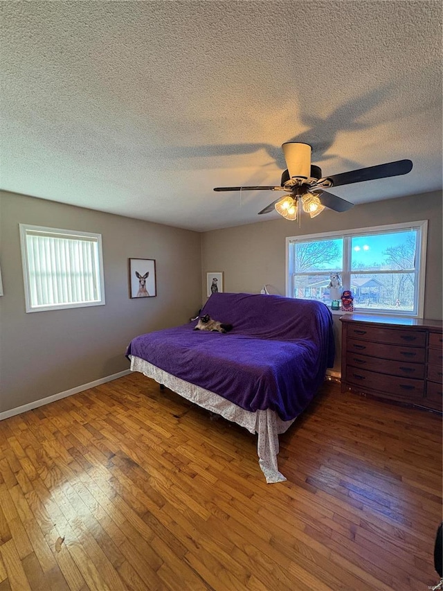 bedroom with a textured ceiling, ceiling fan, hardwood / wood-style floors, and baseboards