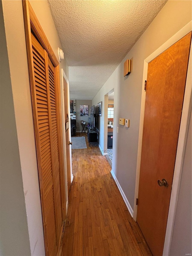 corridor with a textured ceiling, wood-type flooring, and baseboards