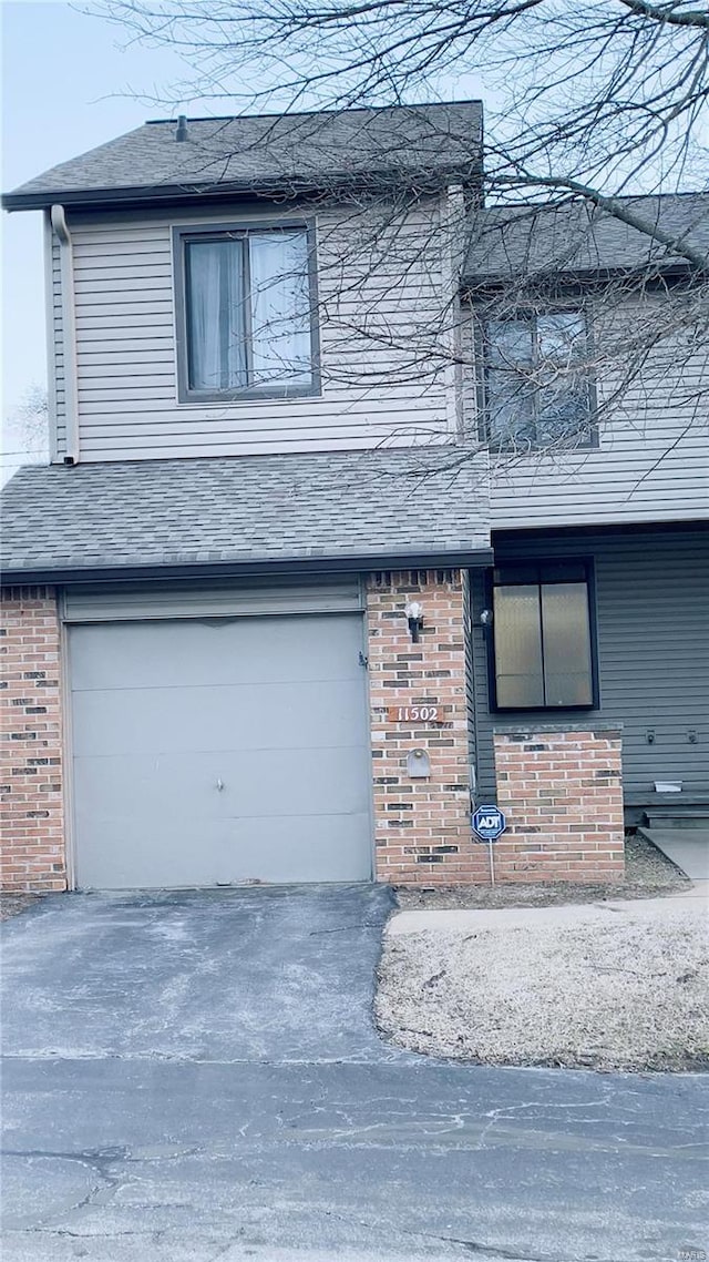 view of front facade featuring a garage, a shingled roof, aphalt driveway, and brick siding