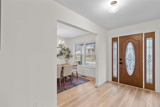 entryway with light wood-type flooring, baseboards, and a textured ceiling