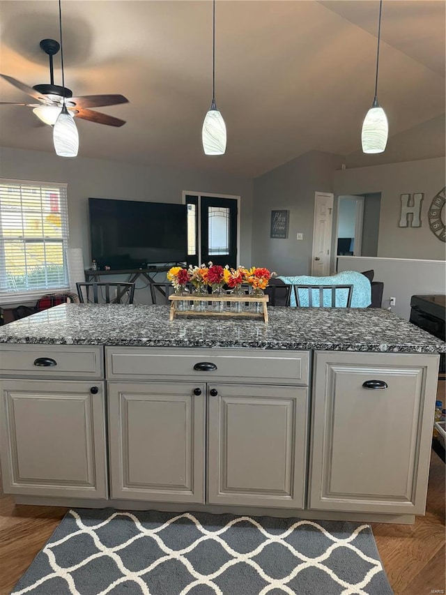 kitchen featuring white cabinets, open floor plan, hanging light fixtures, vaulted ceiling, and stone counters