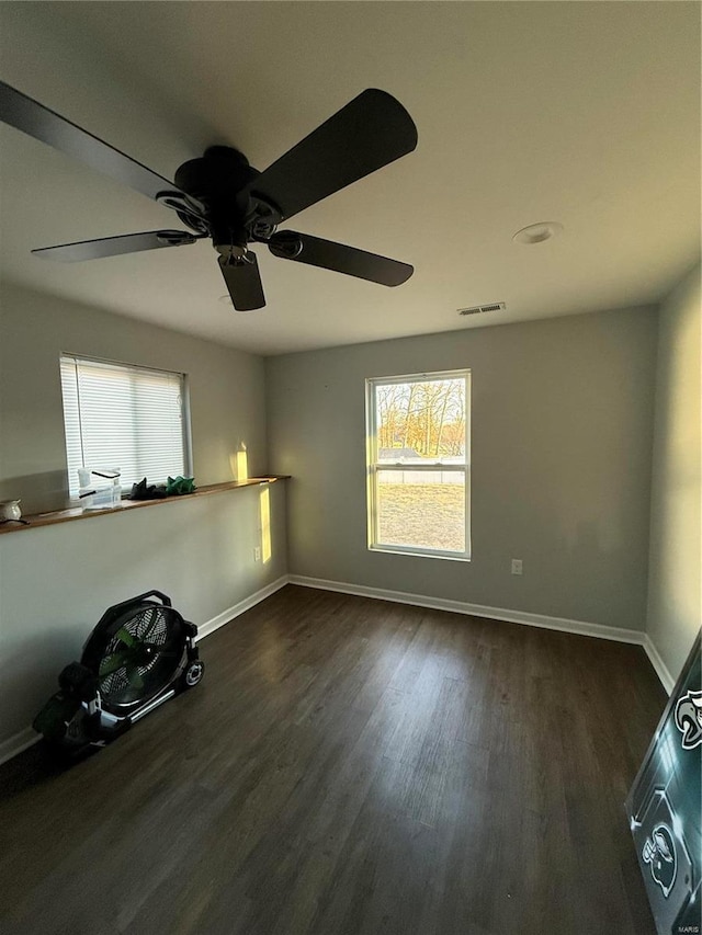 empty room featuring dark wood-type flooring, visible vents, and baseboards