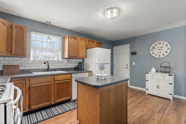 kitchen featuring white appliances, wood finished floors, a sink, tasteful backsplash, and dark countertops