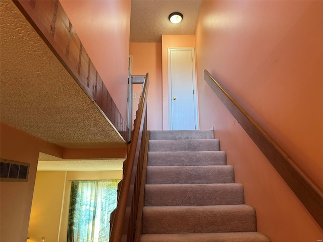 stairway with visible vents and a textured ceiling