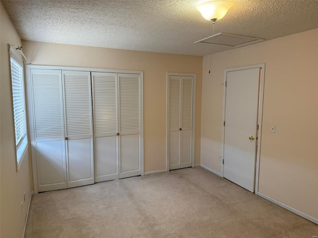 unfurnished bedroom with carpet, multiple closets, attic access, a textured ceiling, and baseboards